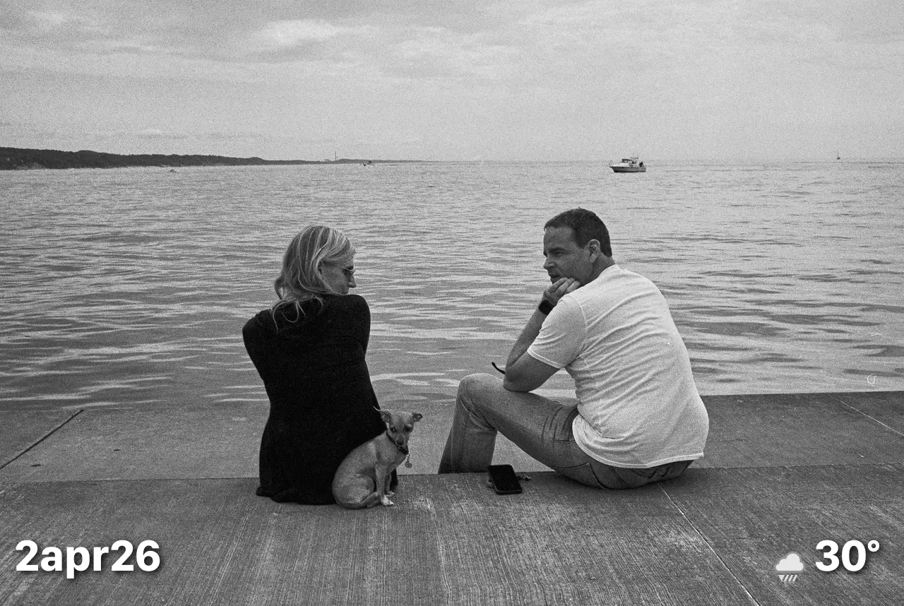 Black and white photo of a couple with small dog sitting on pier