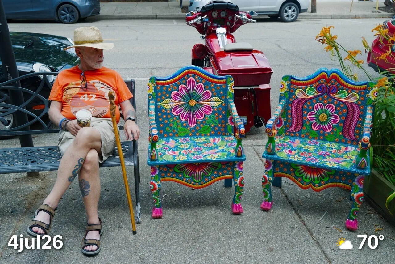 Man sitting on bench next to two colorful chairs