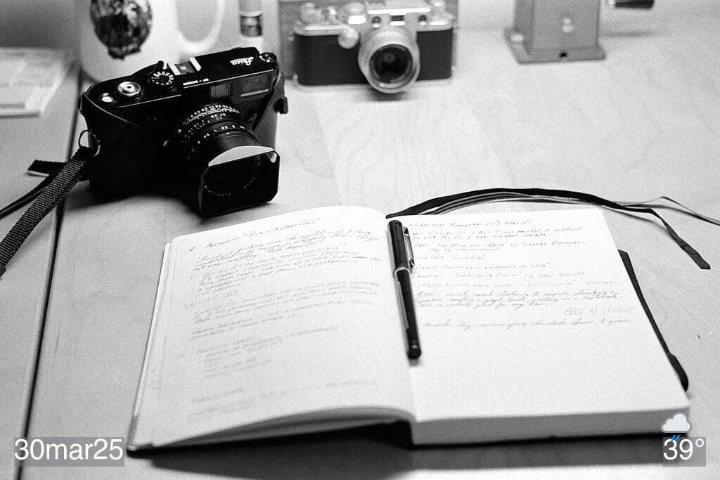 Black and white photo of notebook and camera on desk